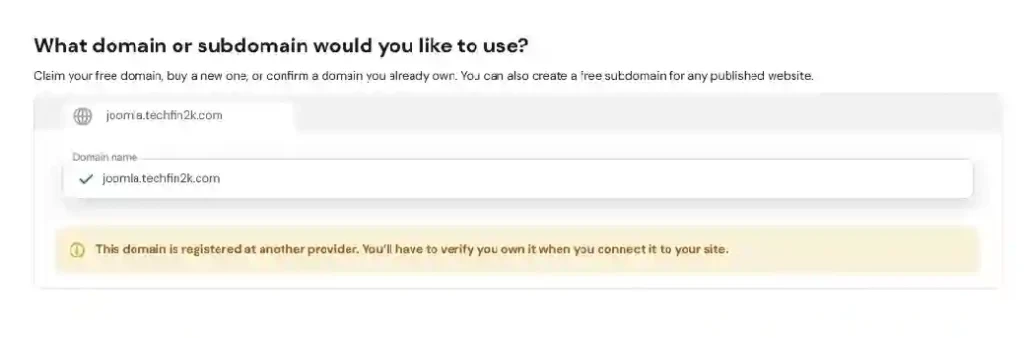 Hostinger showing the domain selection screen with joomla.techfin2k.com and a message indicating the domain is registered with another provider.